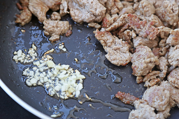 Browned ground chicken pushed aside with minced garlic frying in sesame oil