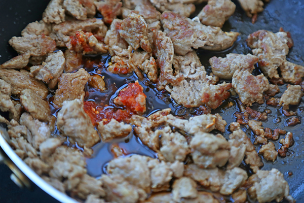 Soy sauce, chili paste, and rice vinegar pooling around ground chicken in a hot skillet