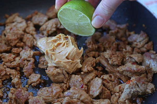 Squeezing lime juice over peanut butter and ground chicken satay in a skillet