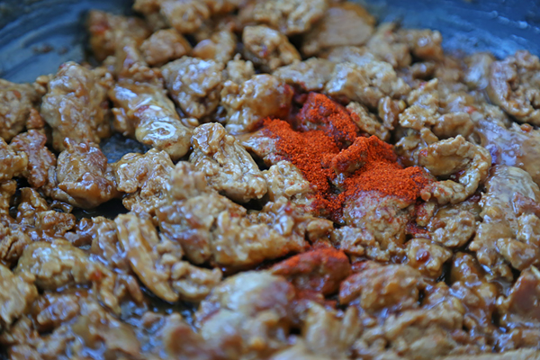 Cayenne pepper and paprika sprinkled over seasoned ground chicken in a skillet