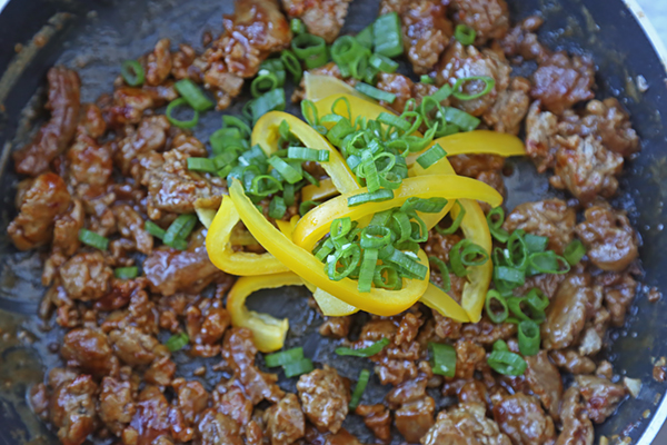 Sliced yellow bell pepper and green onions added to cooked chicken satay