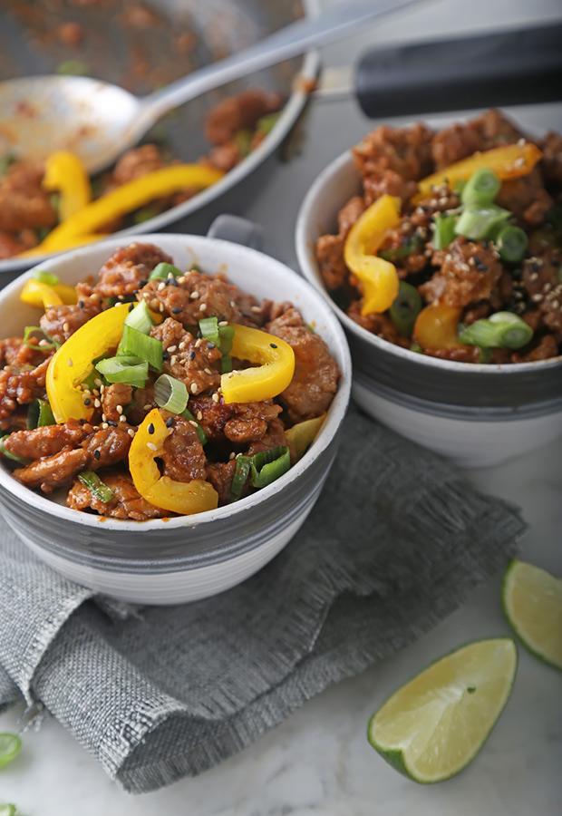 Two bowls of chicken satay topped with sesame seeds, bell pepper, and lime wedges