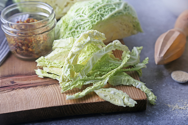 Green cabbage leaves torn into strips on a wooden cutting board with whole grain mustard nearby