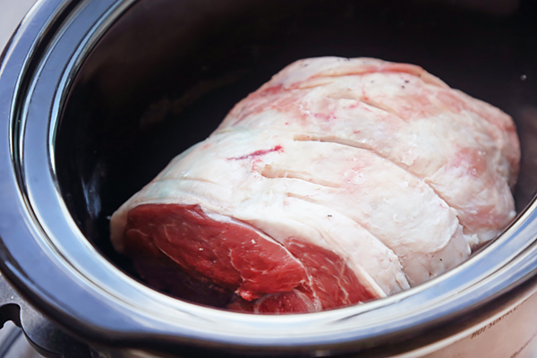 Raw lamb leg with deep slits placed inside a slow cooker