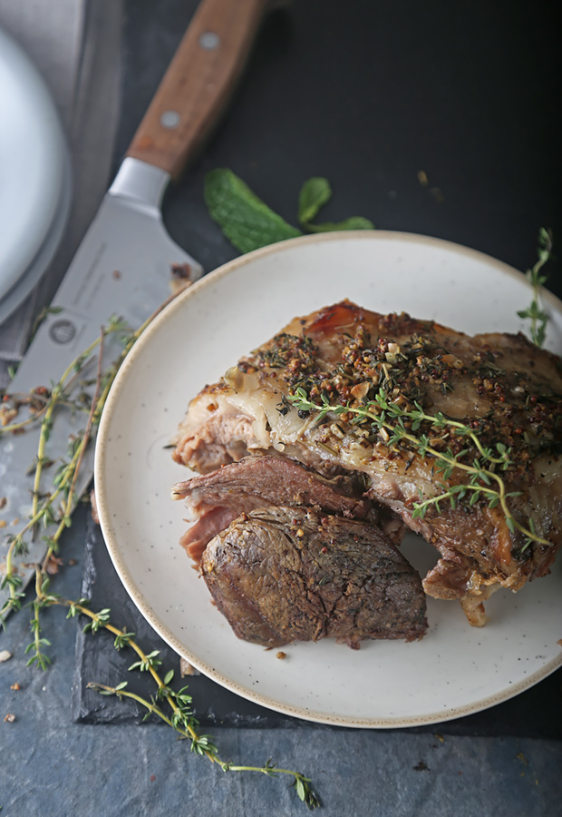Slow-cooked lamb leg sliced on a plate with fresh thyme and mint