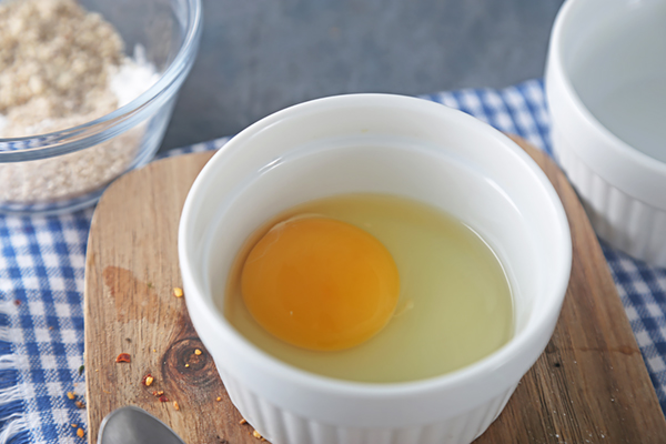 Cracked egg sitting in a white ramekin on a wooden cutting board