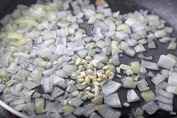 Diced onion and minced garlic sauteing in coconut oil in a dark pan