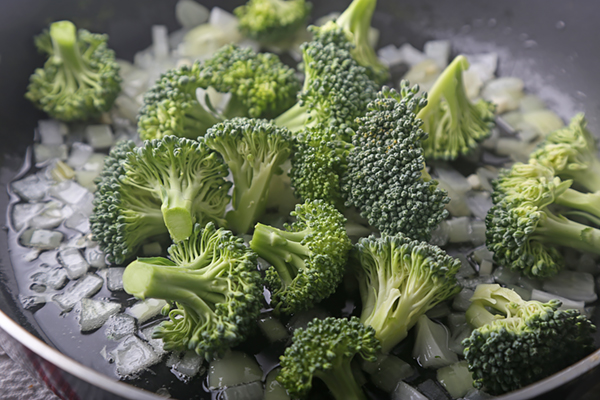 Broccoli florets tossed with sauteed onion and garlic in a skillet