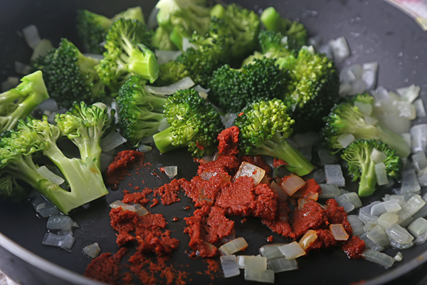 Red curry paste pressed against the pan bottom alongside broccoli and onions