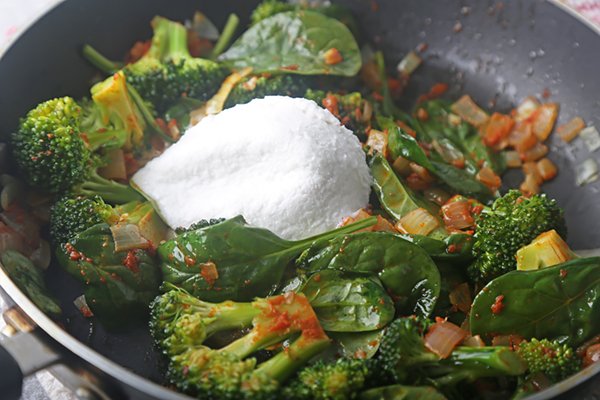 Coconut cream spooned onto wilted spinach, broccoli, and curry vegetables