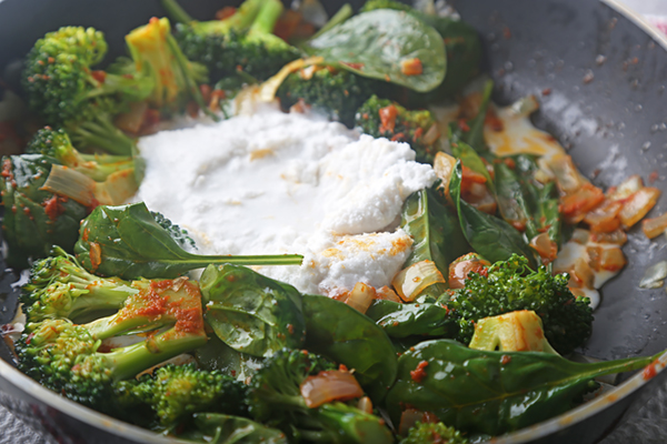 Stirring coconut cream into the broccoli and spinach curry with fish sauce and ginger