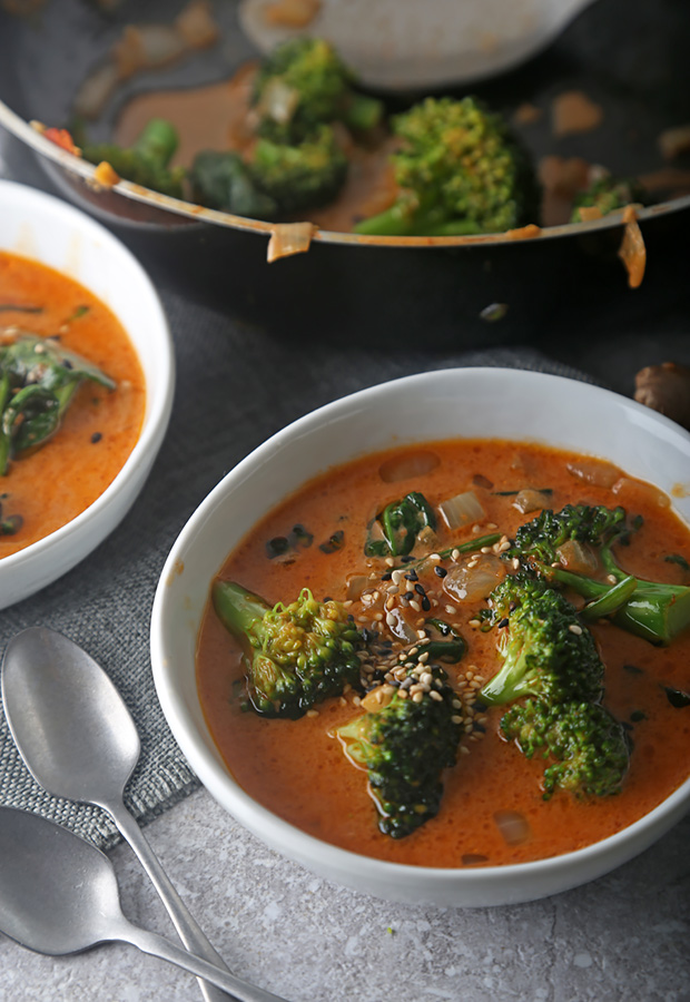 Red coconut curry with broccoli and wilted spinach topped with sesame seeds in white bowls