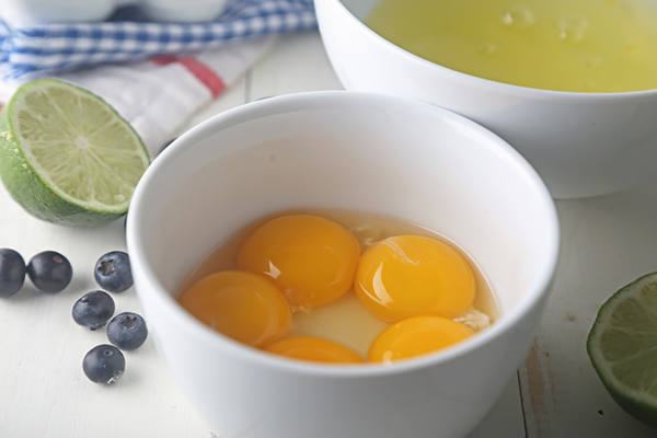 Separated egg yolks in a white bowl with blueberries and lime halves nearby