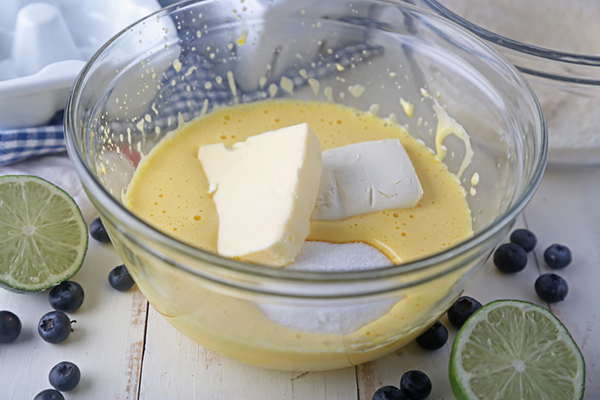Butter, cream cheese, and erythritol added to beaten egg yolks in a glass bowl