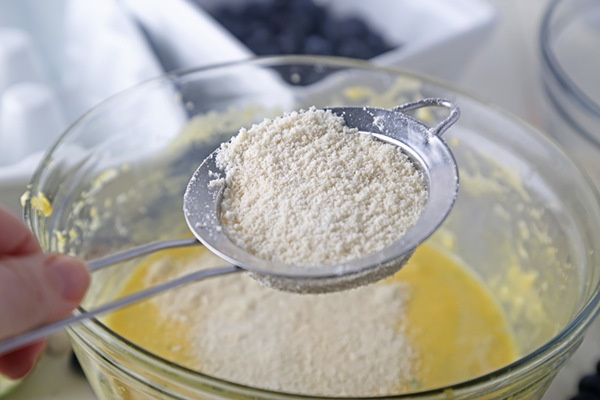 Sifting almond flour and coconut flour through a mesh strainer into the wet batter