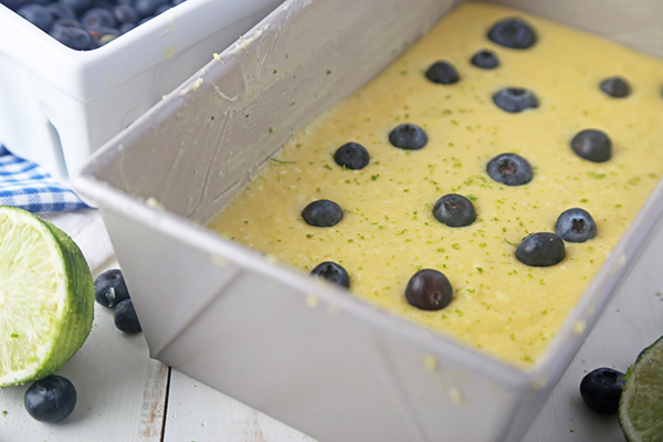 Blueberries scattered over lime cake batter in a white loaf pan