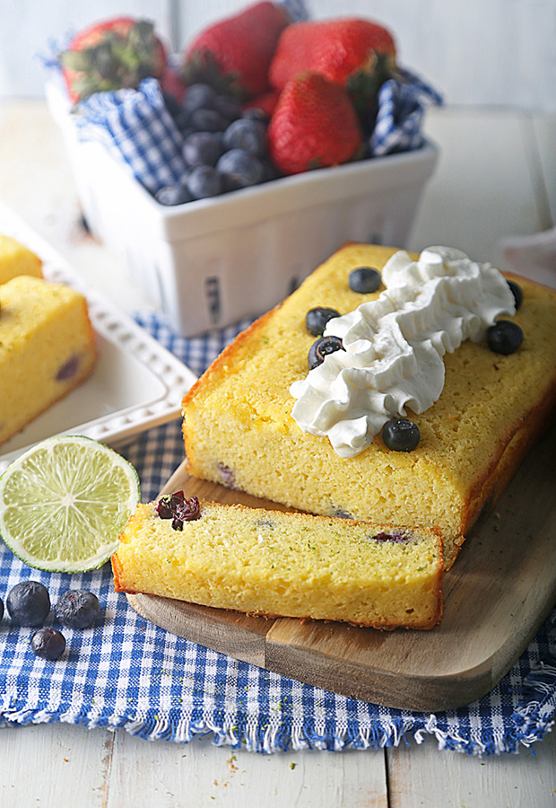 Sliced blueberry lime cake topped with whipped cream on a wooden cutting board