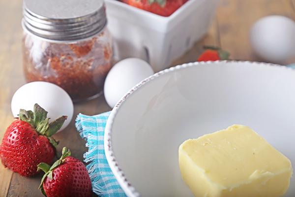 Room temperature butter in a white bowl with eggs, strawberries, and chia seed jam