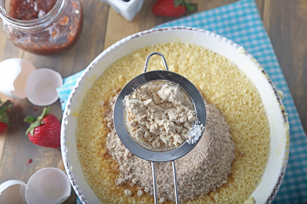 Sifting almond flour, protein powder, and psyllium husk over the wet shortcake batter