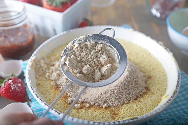 Tapping the mesh strainer to sift dry ingredients into the shortcake batter below
