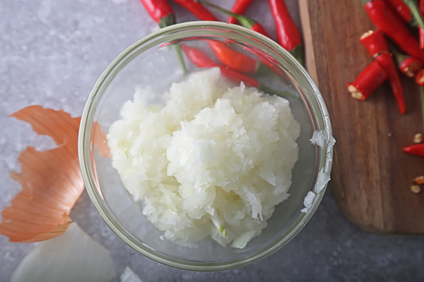 Blended onion paste in a small glass bowl with bird's eye chiles nearby