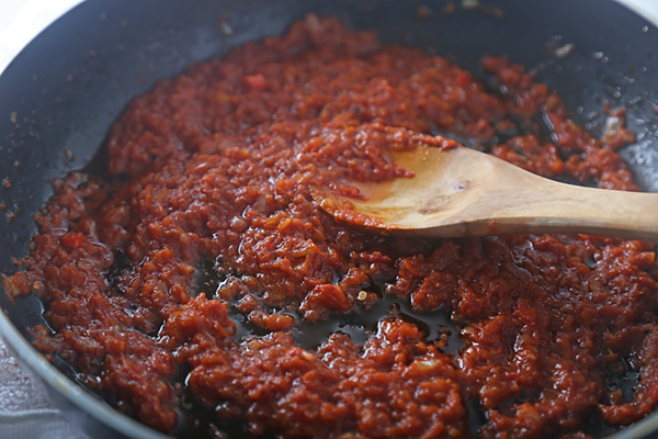 Sambal simmering in a skillet with coconut oil separating from the red sauce