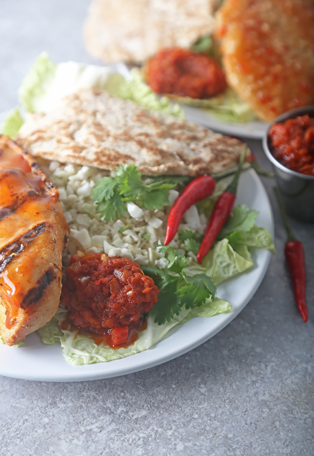 Red sambal spooned over grilled chicken with cauliflower rice, cilantro, and red chiles