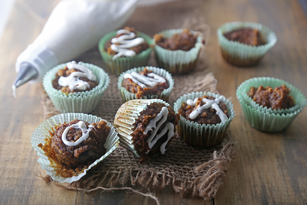 Baked mini pumpkin muffins with cream cheese icing on burlap and wood