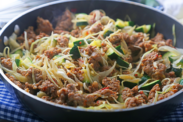 Sauteing shredded cabbage, sliced zucchini, and onion with browned sausage in a skillet