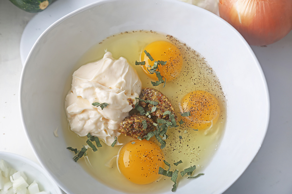 Eggs, mayonnaise, yellow mustard, sage leaves, and cayenne pepper in a white bowl