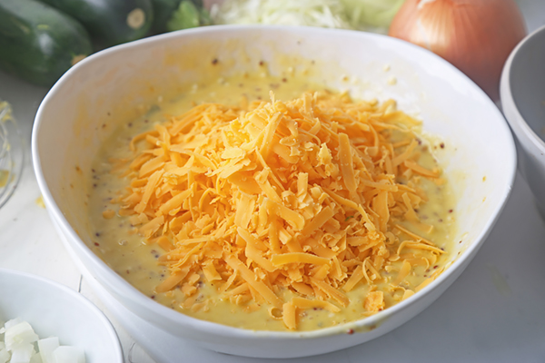 Shredded cheddar cheese piled on top of the whisked egg and mustard mixture