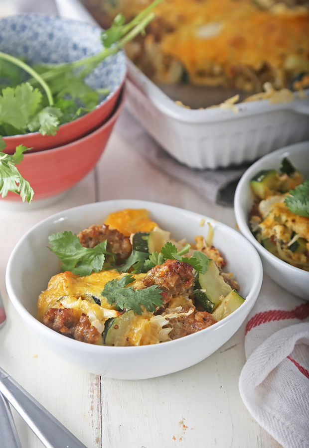 Baked sausage breakfast casserole with melted cheddar, garnished with cilantro in a bowl