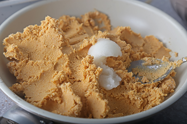 Spooning solid coconut oil into the thick pumpkin and coconut butter mixture