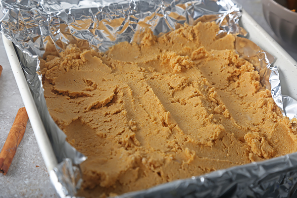 Spreading the thick fudge mixture into a foil-lined square pan with a spoon