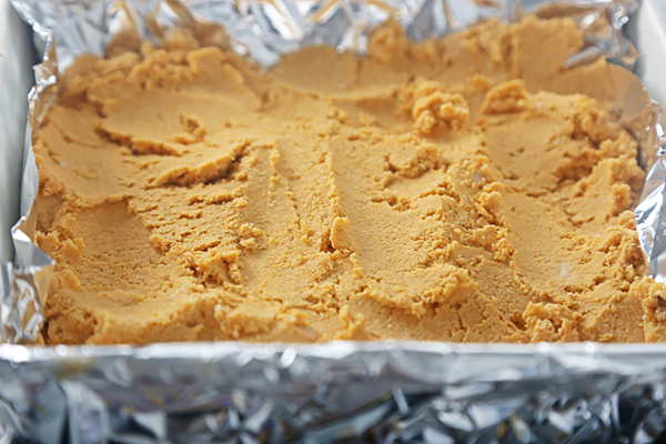 Firm pumpkin fudge in a foil-lined pan after chilling with wax paper removed