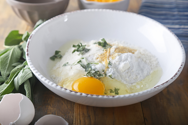 Coconut flour, baking powder, sage, and garlic powder with an egg in a mixing bowl