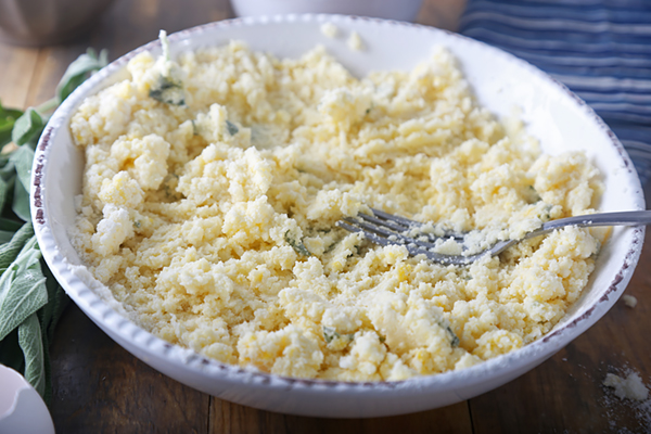 Stiff coconut flour waffle batter with flecks of sage mixed by fork