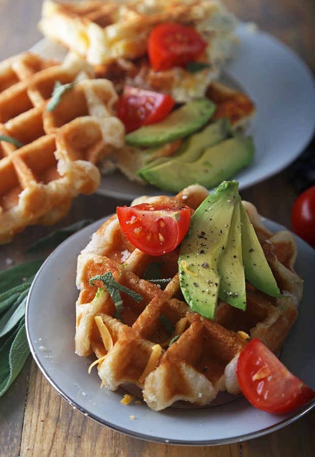 Golden sage and cheddar waffles topped with avocado slices and cherry tomatoes