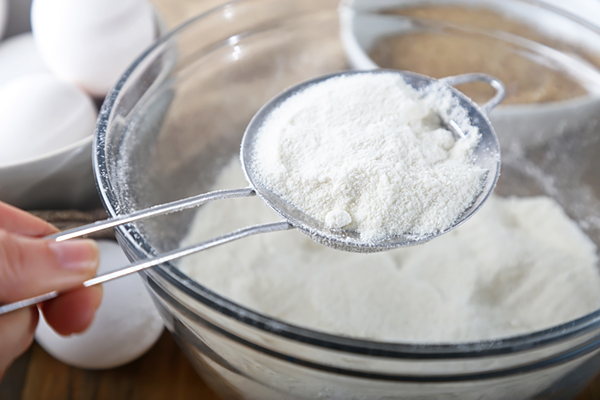 Sifting coconut flour through a fine mesh strainer into a glass mixing bowl