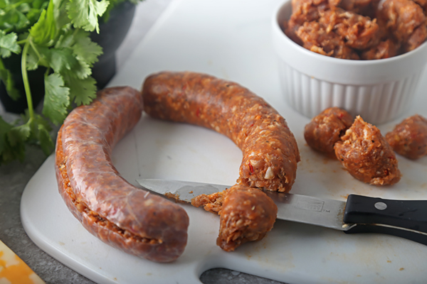 Chorizo sausage being sliced and removed from casing on a white cutting board