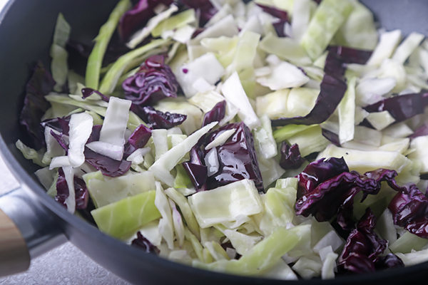 Shredded green and red cabbage with onion sauteing in a skillet