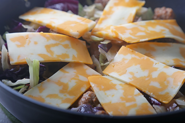 Colby jack cheese slices layered over chorizo, cabbage, and onions in a skillet