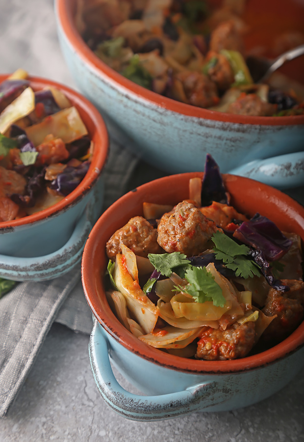 Spicy sausage and cabbage skillet melt served in blue ceramic bowls with cilantro
