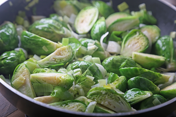 Halved brussels sprouts and sliced leeks sauteing in coconut oil until tender