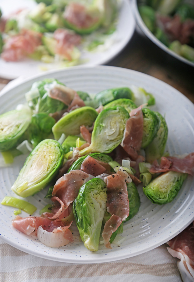 Tender brussels sprouts with wilted leeks and prosciutto served on a speckled plate