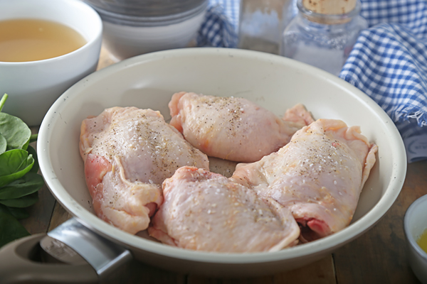Four bone-in skin-on chicken thighs seasoned with salt and pepper in a white skillet