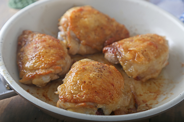 Golden-brown skin-on chicken thighs pan-fried in a white skillet