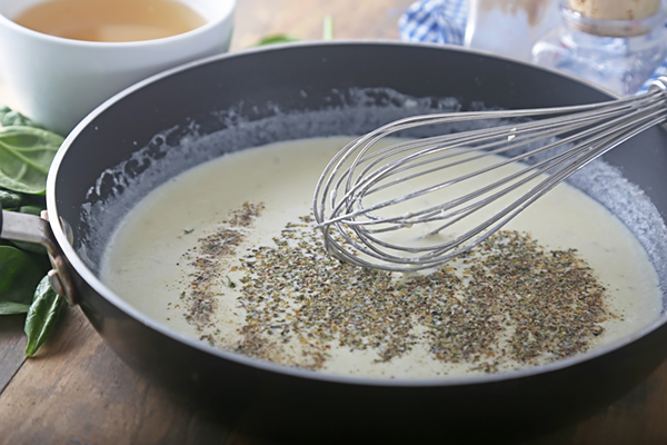 Whisking Italian seasoning into heavy cream sauce in a saucepan