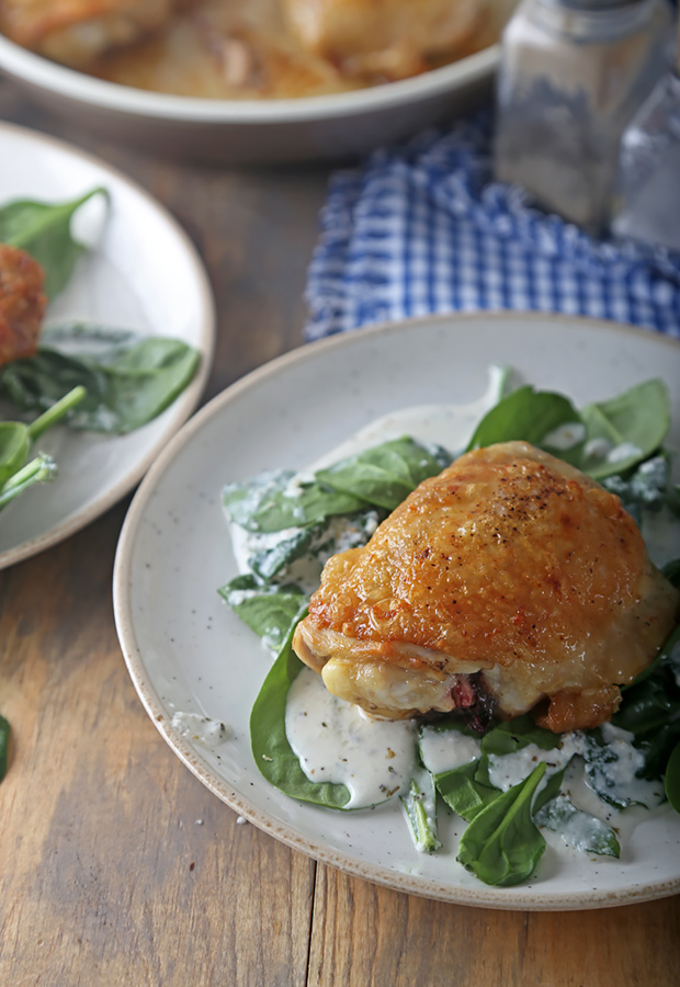 Browned chicken thigh served over creamy spinach on a plate