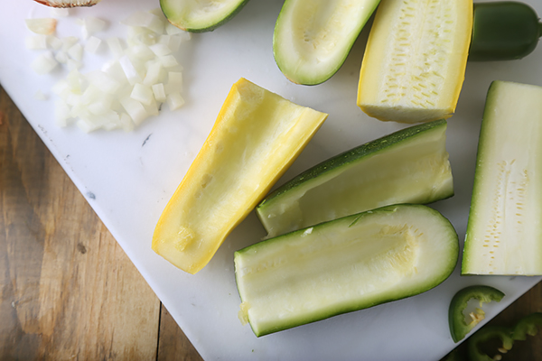 Halved zucchini scooped out on a cutting board with diced onion and jalapeno